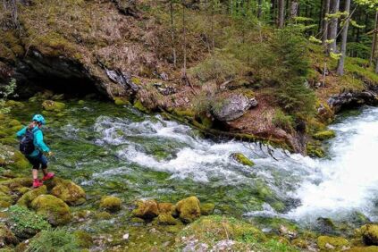 Eine Frau geht auf den großen Steinen zu einen Bach im Wald