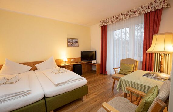 A double bed and two chairs with a table are in the hotel room of the Landhotel Agathawirt
