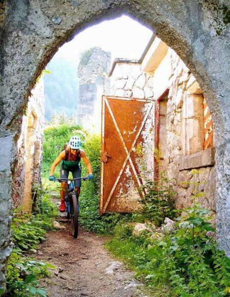 Eine Frau fährt mit dem Bike unter einer Ruine durch