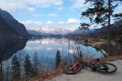 Ein Fahrrad liegt am Ufer des Hallstättersees, die weißen Berge und der blaue Himmel spiegeln sich darin