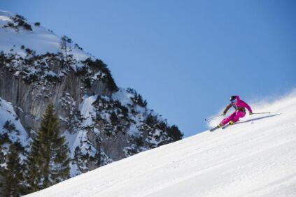 Eine Skifahrerin im pinken Skianzug fährt die frische Piste hinab