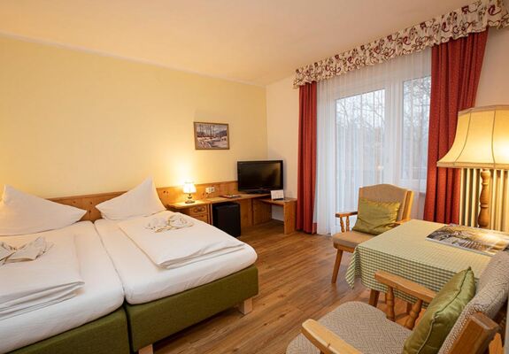 Ein Doppelbett und zwei Stühle mit einem Tisch befinden sich im Hotelzimmer des Landhotel Agathawirt
