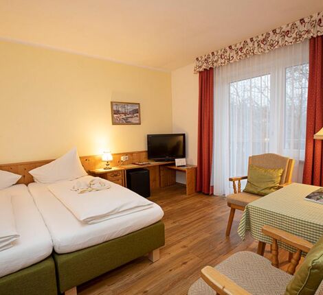 Ein Doppelbett und zwei Stühle mit einem Tisch befinden sich im Hotelzimmer des Landhotel Agathawirt