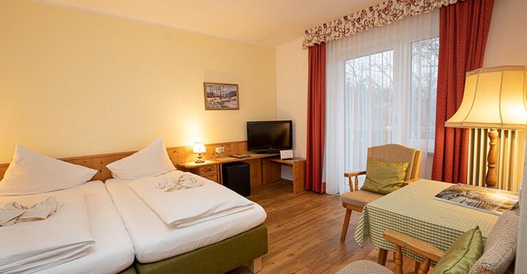 Ein Doppelbett und zwei Stühle mit einem Tisch befinden sich im Hotelzimmer des Landhotel Agathawirt