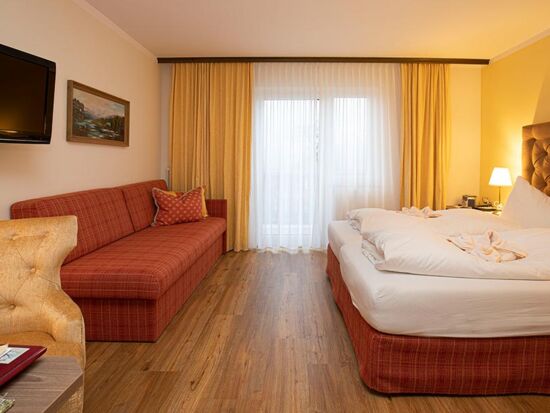 A hotel room at Hotel Agathawirt with a double bed, a red sofa and a TV set