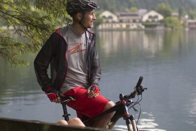 Eine Frau liegt auf der Parkbank am See und neben ihr sitzt ein Mann auf seinem Mountainbike
