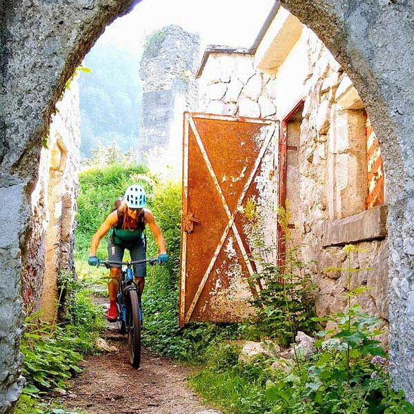 Eine Frau fährt mit dem Bike unter einer Ruine durch