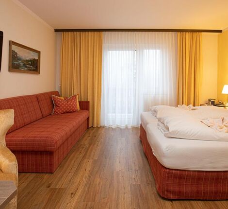 Ein Hotelzimmer im Hotel Agathawirt mit einem Doppelbett, einem roten Sofa  und einem Fernseher
