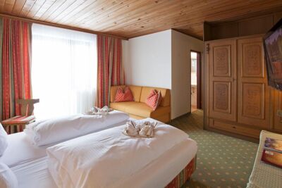 Ein Doppelbett mit weißer Bettdecke und einer kleinen Couch. Gegenüber vom Bett ist ein großer brauner Schrank