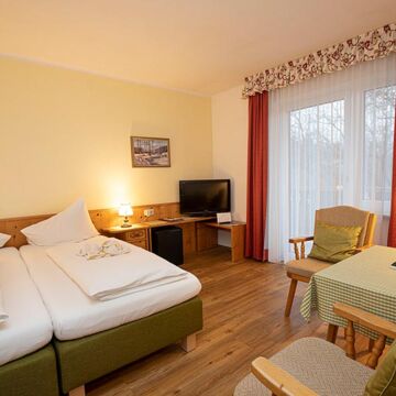 Ein Doppelbett und zwei Stühle mit einem Tisch befinden sich im Hotelzimmer des Landhotel Agathawirt