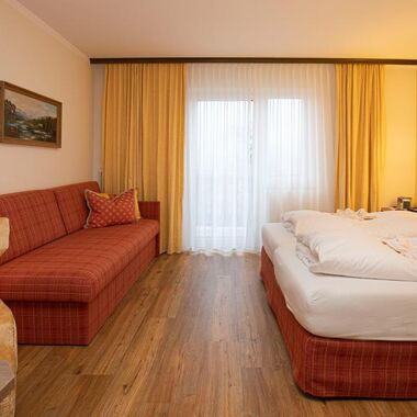 Ein Hotelzimmer im Hotel Agathawirt mit einem Doppelbett, einem roten Sofa  und einem Fernseher