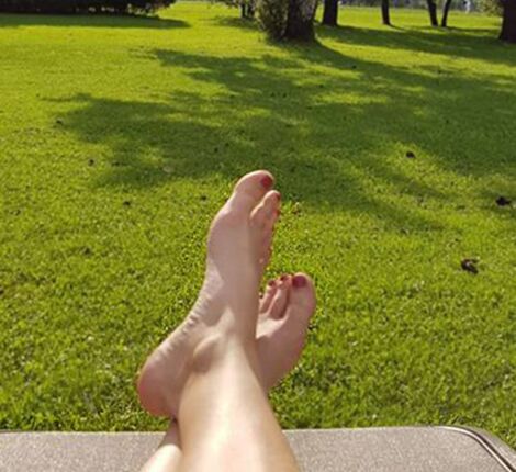 Eine Frau legt ihre Füße auf der Liege im Garten hoch