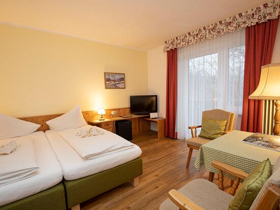Ein Doppelbett und zwei Stühle mit einem Tisch befinden sich im Hotelzimmer des Landhotel Agathawirt