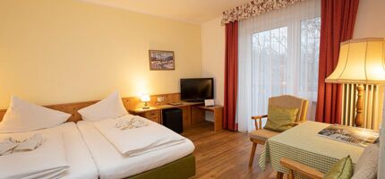 A double bed and two chairs with a table are in the hotel room of the Landhotel Agathawirt