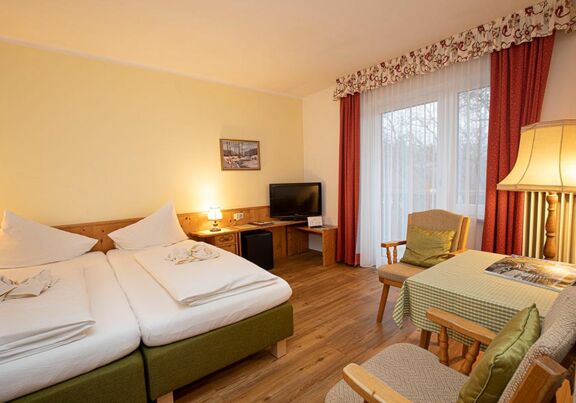 Ein Doppelbett und zwei Stühle mit einem Tisch befinden sich im Hotelzimmer des Landhotel Agathawirt