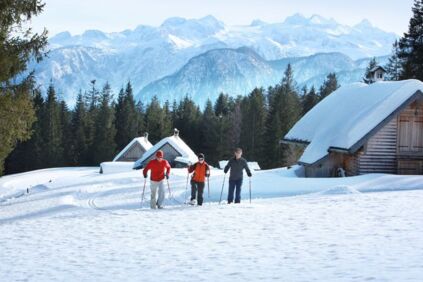 Drei Schneeschuhwanderer passieren ein Hüttendorf neben der Piste