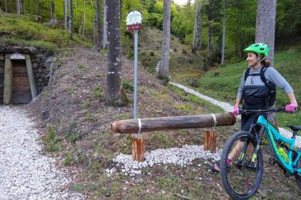 Eine Frau steht auf einem Weg mitten im Wald mit ihrem Mountainbike