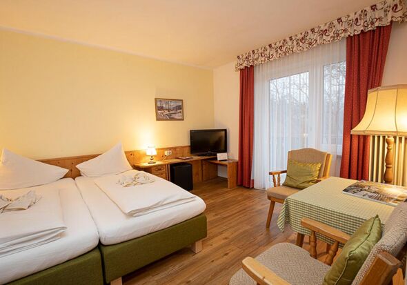 Ein Doppelbett und zwei Stühle mit einem Tisch befinden sich im Hotelzimmer des Landhotel Agathawirt