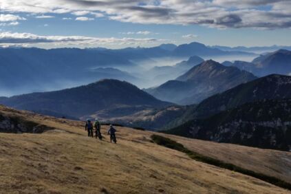 Drei Biker fahren im Herbst den Berg hinab, und blicken hinunter ins Nebelbedeckte Tal