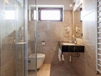Badezimmer mit hellen Marmorfliesen und begehbarer Dusche im Hotel Agathawirt